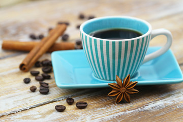 Cup of black coffee in vintage cup, star anise, cinnamon sticks and scattered coffee beans on wooden surface
