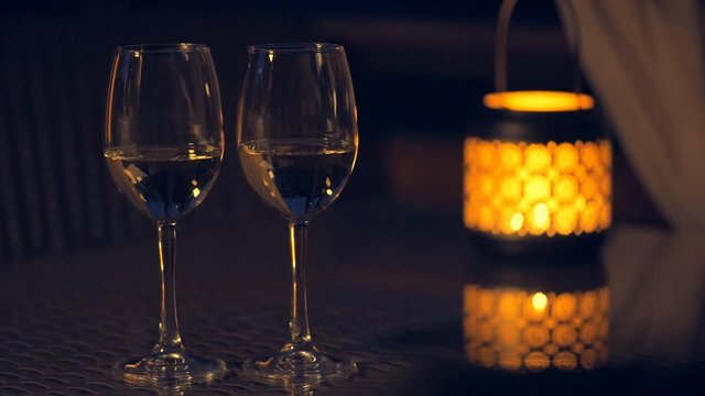 Cinemagraph - Two white wine wineglasses with  lantern with lighted candle on table. Concept of romance. Motion Photo.