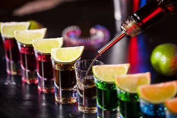 Rolgordijnen Bartender pouring alcoholic drink into small glasses on bar. Colorful cocktails at the bar. © nikilitov