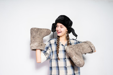 a laughing young Russian girl in a black fur hat rejoices in winter, holds gray felt boots