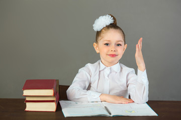 beautiful little girl with a bow on her head sitting at a desk with books on a gray background