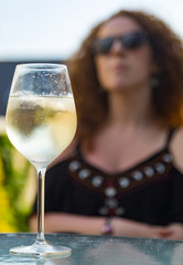 Glass of chilled white wine on a table outdoors during summer, out of focus woman in the background