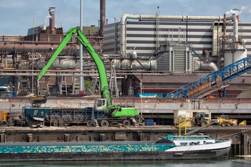 Big steel factory in harbor IJmuiden with crane unloading a barge, The Netherlands.