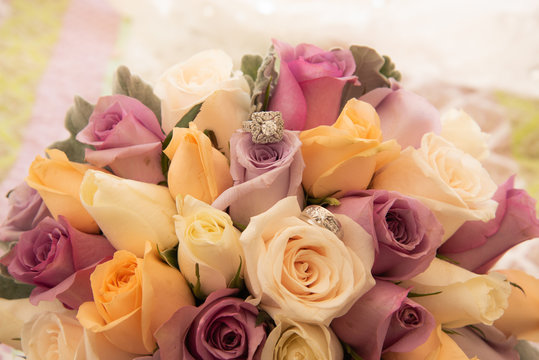 Beautiful toned picture with diamond wedding rings lying on top of a colorful bouquet of roses