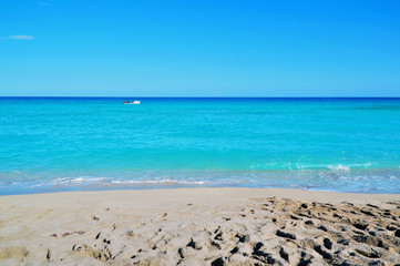 coastline of the ocean, small waves, horizon, endless distance, white motor boat with silhouettes of people in the ocean, against a blue sky covered with sparse clouds Cuba