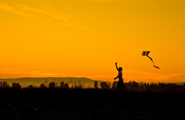 Silhouette Girl playing kite in the field. At sunrise