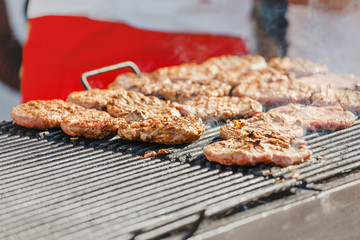 Chef cooks on the street preparing beef cutlet and bread on the grill for hamburgers