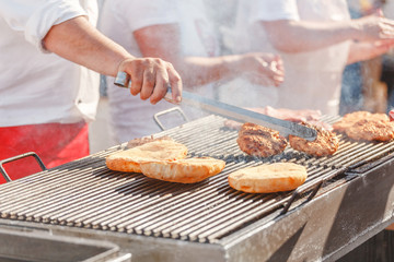 Chef cooks on the street preparing beef cutlet and bread on the grill for hamburgers