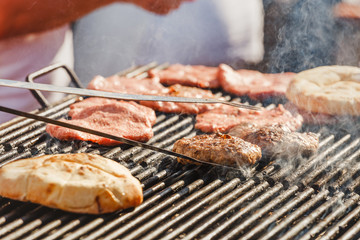 Chef cooks on the street preparing beef cutlet and bread on the grill for hamburgers