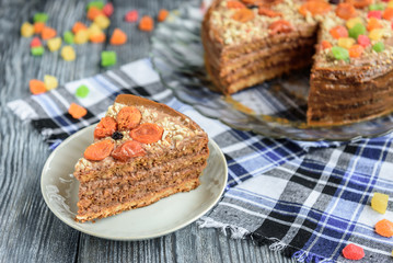 Homemade air-nut cake with chocolate cream, boiled condensed milk, candied fruit, nuts and dried apricot on grey wooden background.