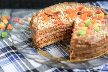 Homemade air-nut cake with chocolate cream, boiled condensed milk, candied fruit, nuts and dried apricot on grey wooden background.