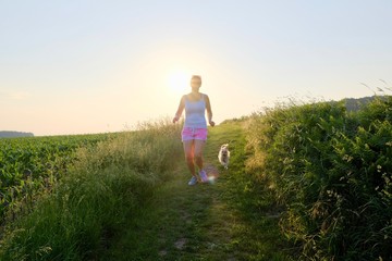 Woman Silhouette with a dog running down a gravel path at sunset