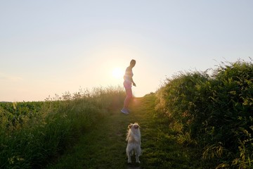 Woman Silhouette with a dog walking up a gravel path at sunset