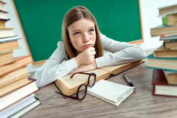 Boredom. Schoolgirl resting her chin on her hands, laying on a table with opened book. Creative concept with Back to school theme