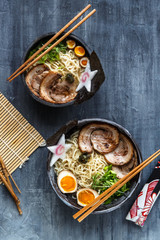 Two ramen bowls with pork, egg and chives, top view