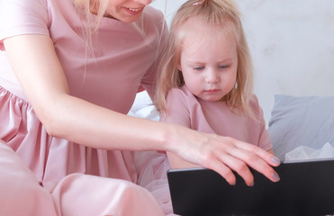 Charming little blond girl watching a video on tablet with her mom.