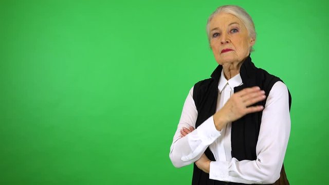 An elderly woman looks seriously at the camera - green screen studio