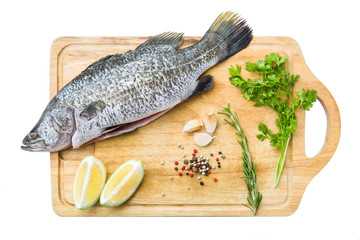 Raw fish with lemon, herbs and garlic on wooden cutting board, isolated white background
