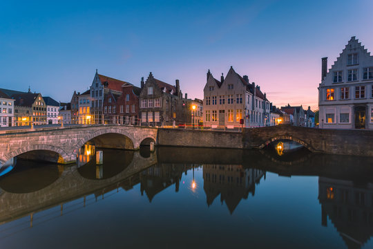 Dusk lights on the historic buildings of the city centre reflected in the typical canals Bruges West Flanders 