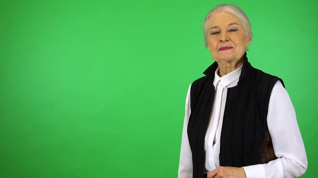 An elderly woman smiles and waves at the camera - green screen studio