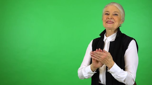 An elderly woman applauds and smiles at the camera - green screen studio