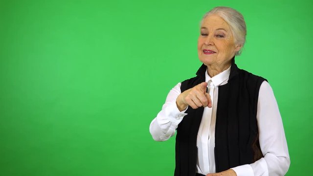 An elderly woman points at the camera and smiles - green screen studio