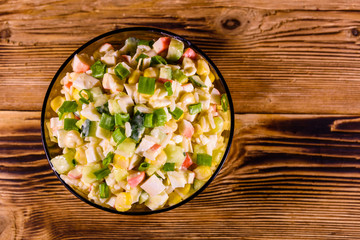 Glass bowl with salad from crab sticks on wooden table. Top view