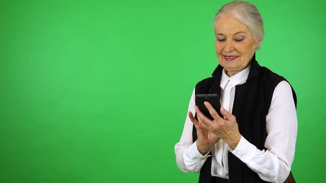An elderly woman works on a smartphone with a smile - green screen studio