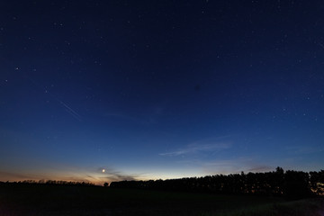 Bright star-planet Venus over the field and forest against the starry sky at dusk.