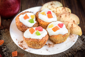 Oat muffins with yogurt, candied fruit, red apple and cinnamon on dark wooden background.