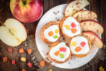 Oat muffins with yogurt, candied fruit, red apple and cinnamon on dark wooden background.