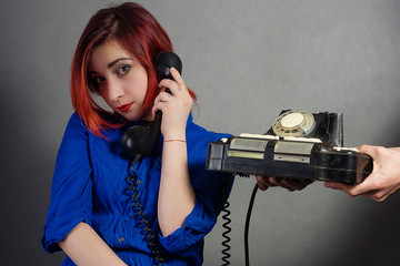 A girl with red hair in a blue dress with a cigarette rings an old phone