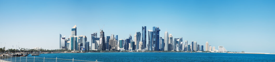 The morning panoramic view of the skyscrapers of Doha from the Persian Gulf. Futuristic skyline in the financial district of Qatar in the early morning and embankment with moored ships
