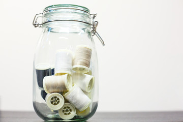 glass transparent jar with spools of thread inside