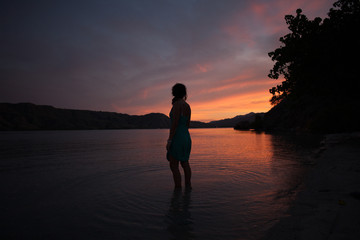 Woman in a blue dress looking out at sunset