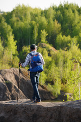 Photo from back of young tourist with walking sticks on hill on background of vegetation