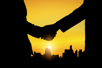 Obraz premium silhouette of business people team and successful teamwork group staning on top of boulding and shaking hand in summer sunset