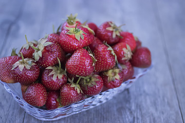 Ripe strawberries in a glass plate on a gray background.