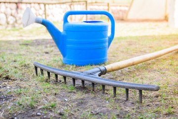 Garden rakes and watering can on the grass in the spring or summer garden.