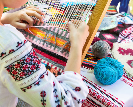 Hands of a girl weaving a Ukrainian mat made of multi-colored threads.
