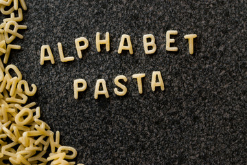 Raw Alphabet Pasta is Written with Letters  on Granit Grey Surface.