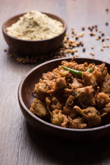 Chick pea flour or Besan powder in a ceramic or wooden bowl along with fried onion pakora or kanda bajji