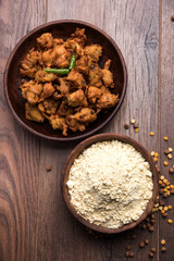 Chick pea flour or Besan powder in a ceramic or wooden bowl along with fried onion pakora or kanda bajji
