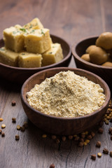 Chick pea flour or Besan powder in a ceramic or wooden bowl along with Gujrati Dhokla snack, onion bajji or bhaji and sweet laddu or laddoo