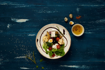 Tasty vegetarian salad made of quail eggs, lettuce, Feta cheese, broccoli, cauliflower, olives and baby corn on plate standing on blue old wooden table. Healthy dietary meal, wholesome dish. Top view.