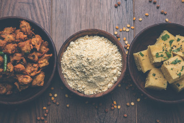 Chick pea flour or Besan powder in a ceramic or wooden bowl along with Gujrati Dhokla snack, onion bajji or bhaji and sweet laddu or laddoo