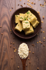 Chick pea flour or Besan powder in a ceramic or wooden bowl along with Gujrati Dhokla snack