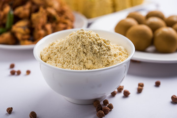 Chick pea flour or Besan powder in a ceramic or wooden bowl along with Gujrati Dhokla snack, onion bajji or bhaji and sweet laddu or laddoo
