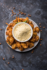 Chick pea flour or Besan powder in a ceramic or wooden bowl along with fried onion pakora or kanda bajji