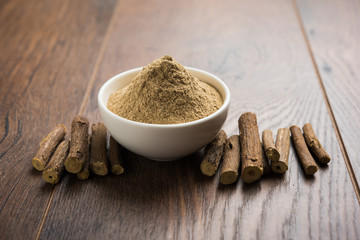 Ayurvedic Mulethi or Liquorice root stick or jeshthamadh powder served in a bowl over moody background